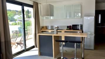A modern kitchen with a central island, bar stools, a refrigerator, and a microwave.