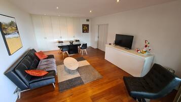 A modern living room with a black leather sofa, a round coffee table, and a TV on a white stand.