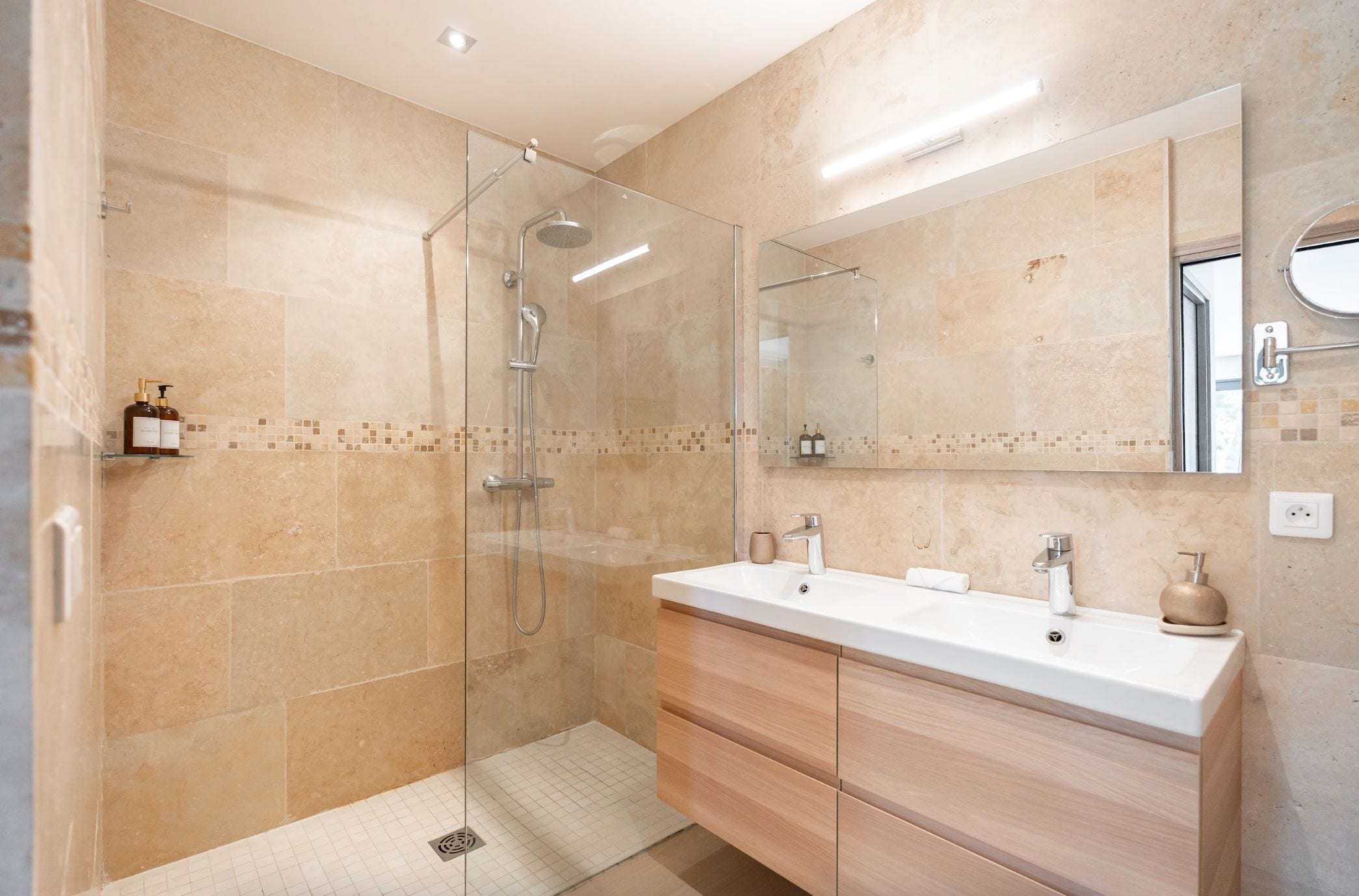 Un baño moderno con ducha envuelta en vidrio, tocador doble y un espejo grande.