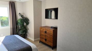 Una habitación de hotel con una cama, un tocador de madera, una planta en maceta y un televisor de pantalla plana montado en la pared.