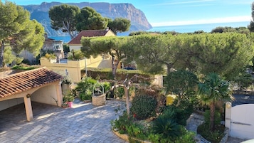 A courtyard with a pergola, potted plants, and a view of the sea and mountains.