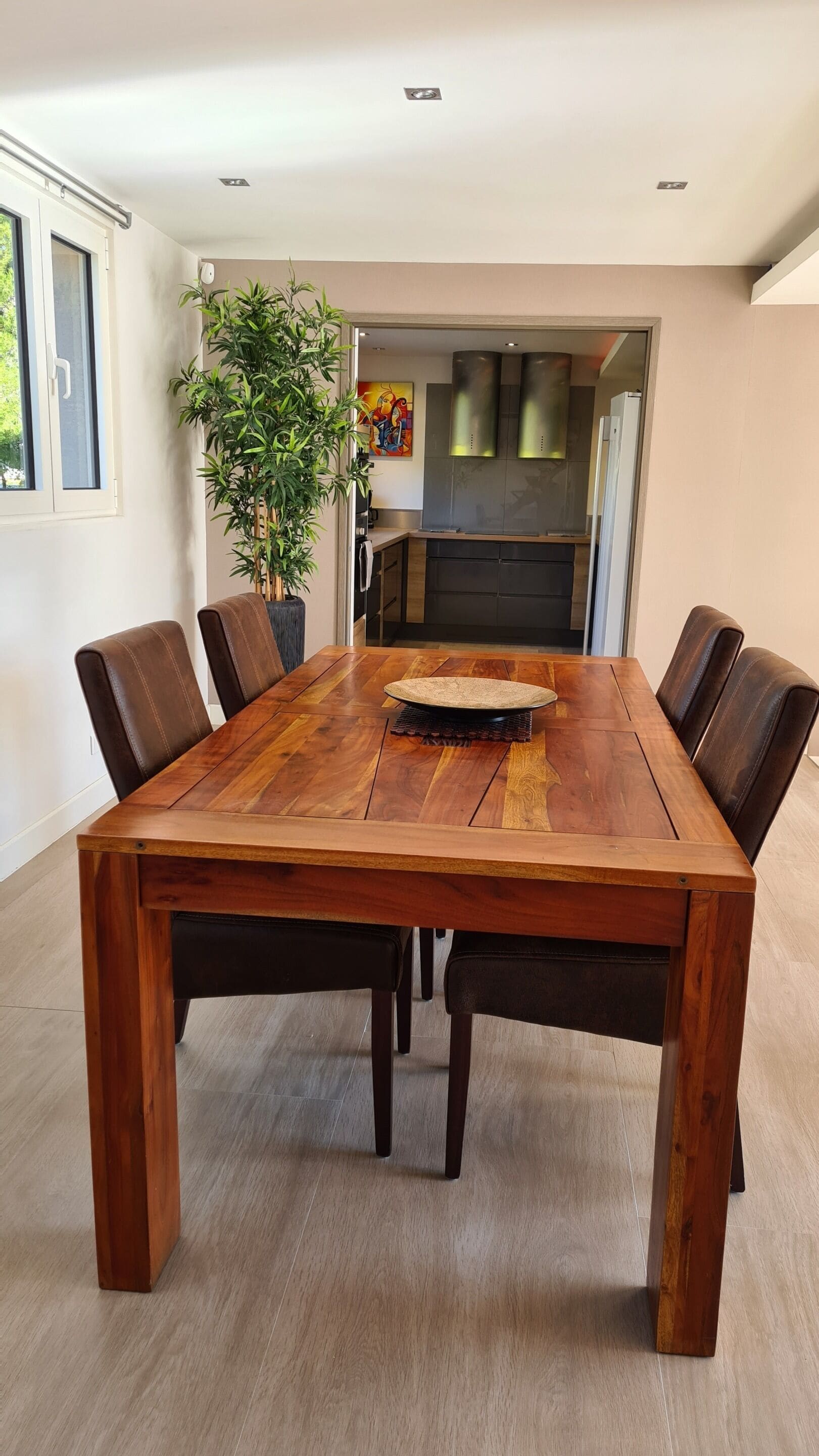 Ein Essbereich mit einem großen Holztisch, sechs Stühlen, einer Topfpflanze und einer Küche im Hintergrund.