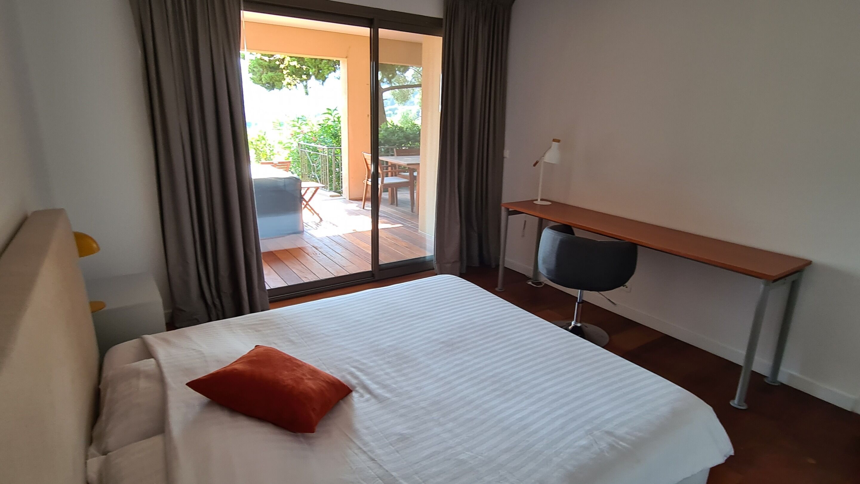 A bedroom with a bed, a desk, and a view of an outdoor patio.