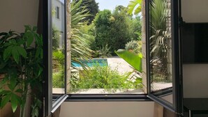 A window with a view of a garden, a pool, and a building in the background. - Hôtel Particulier Cassis, Parking sécurisé, Piscine chauffée (Cassis)