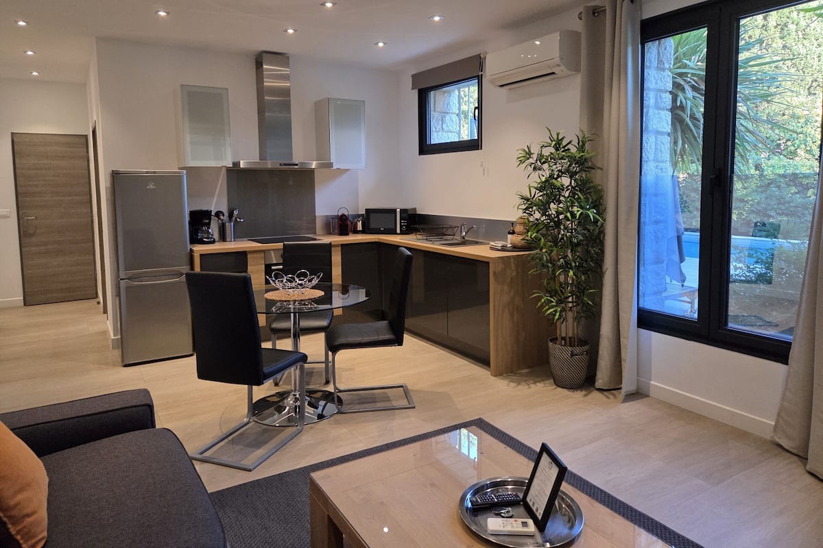 A modern kitchen with a dining area, a refrigerator, a microwave, and a large window with a view of greenery.
