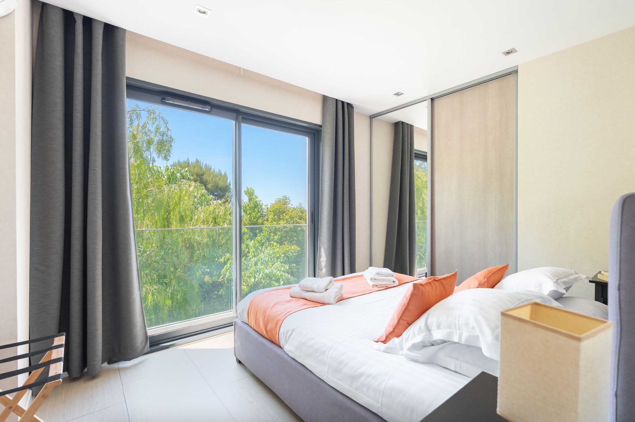 Un dormitorio moderno con un ventanal grande, una cama con almohadas y una mesita de noche.
