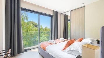 Un dormitorio moderno con un ventanal grande, una cama con almohadas y una mesita de noche.