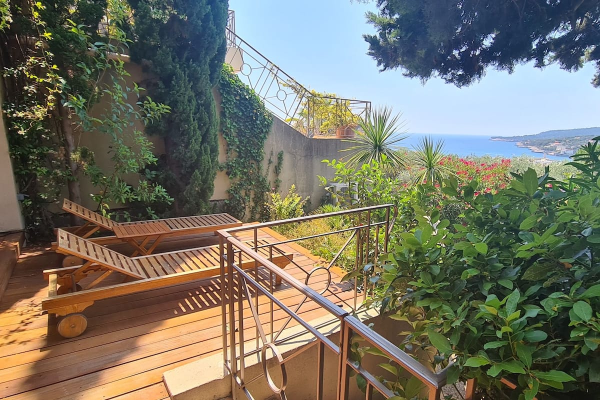 A wooden deck with outdoor furniture, a metal railing, and lush greenery.