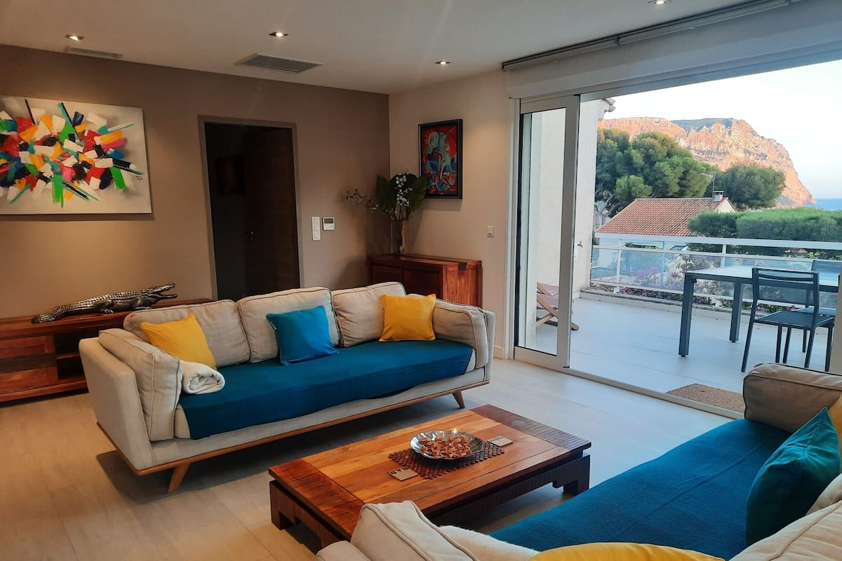 A modern living room with a sofa, coffee table, and a view of a mountainous landscape through large sliding glass doors.
