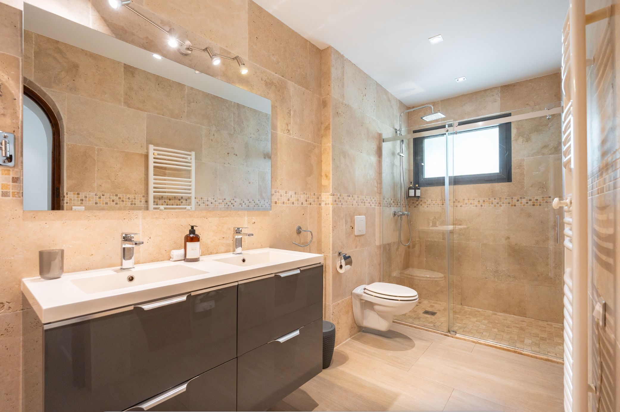 A modern bathroom with a glass-enclosed shower, a double sink vanity, and a toilet.