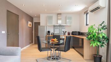 A modern kitchen with a dining area, a potted plant, and a grey sofa.