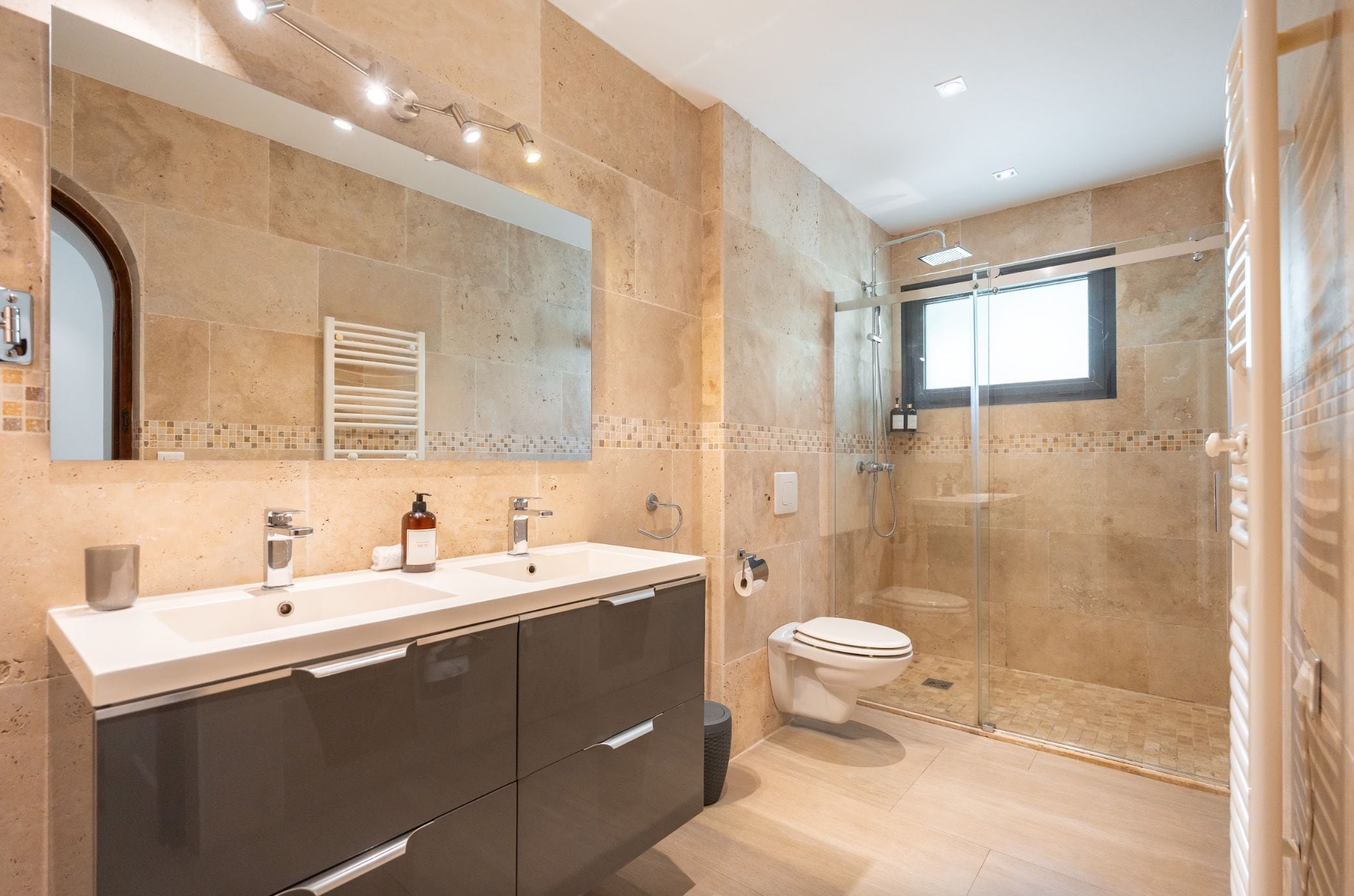 A modern bathroom with a glass-enclosed shower, a double sink vanity, and a toilet.