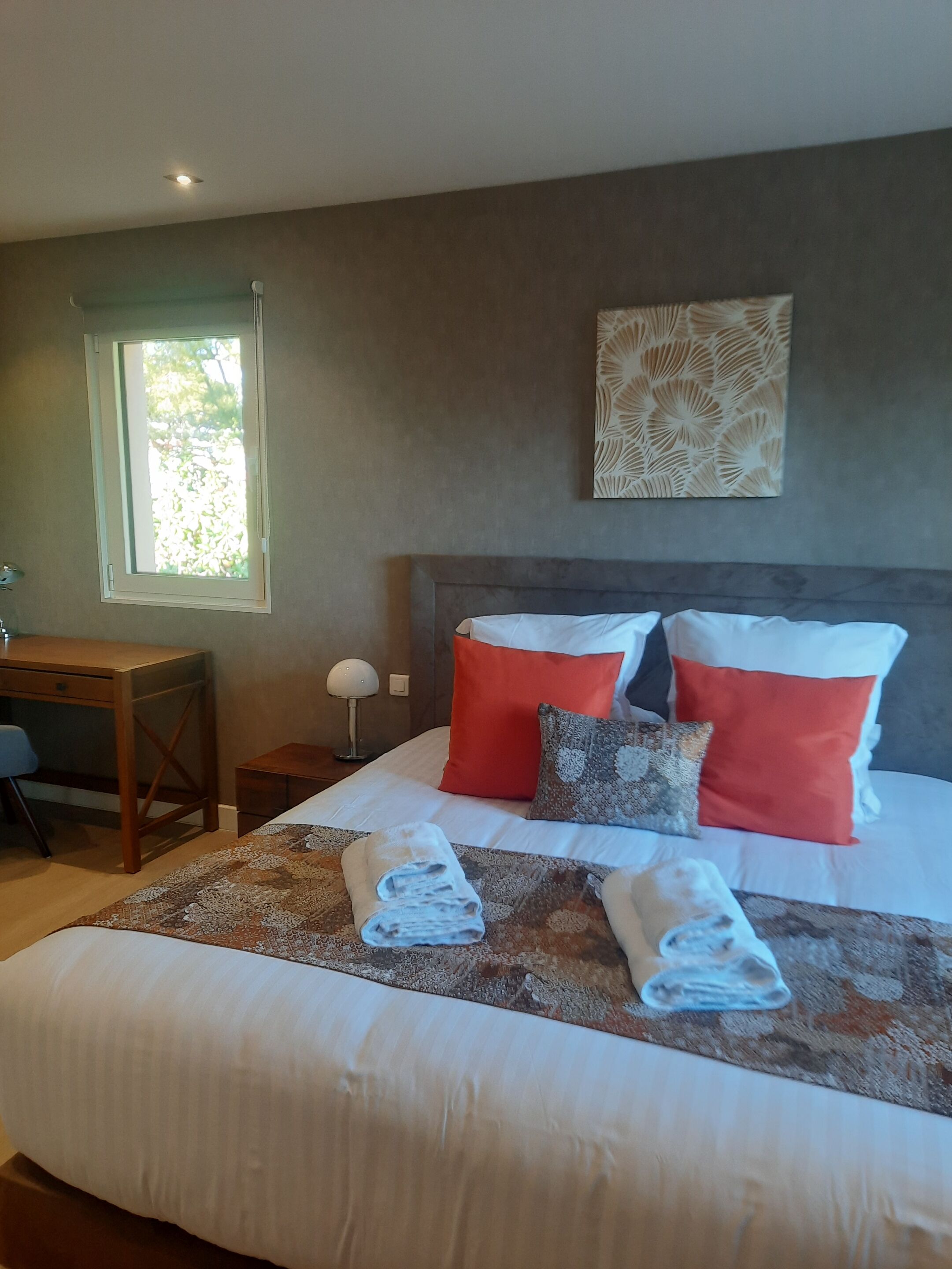 A hotel room with a bed, a desk, a chair, a lamp, and a window.