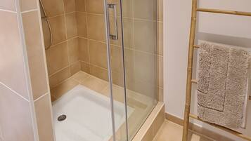 A shower with a glass door, a towel rack with a towel, and a wooden ladder.