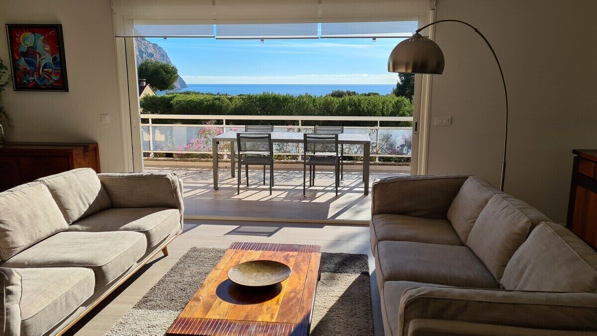 Un salon avec deux canapés, une table basse et une vue sur la mer, visible à travers une porte-fenêtre coulissante.