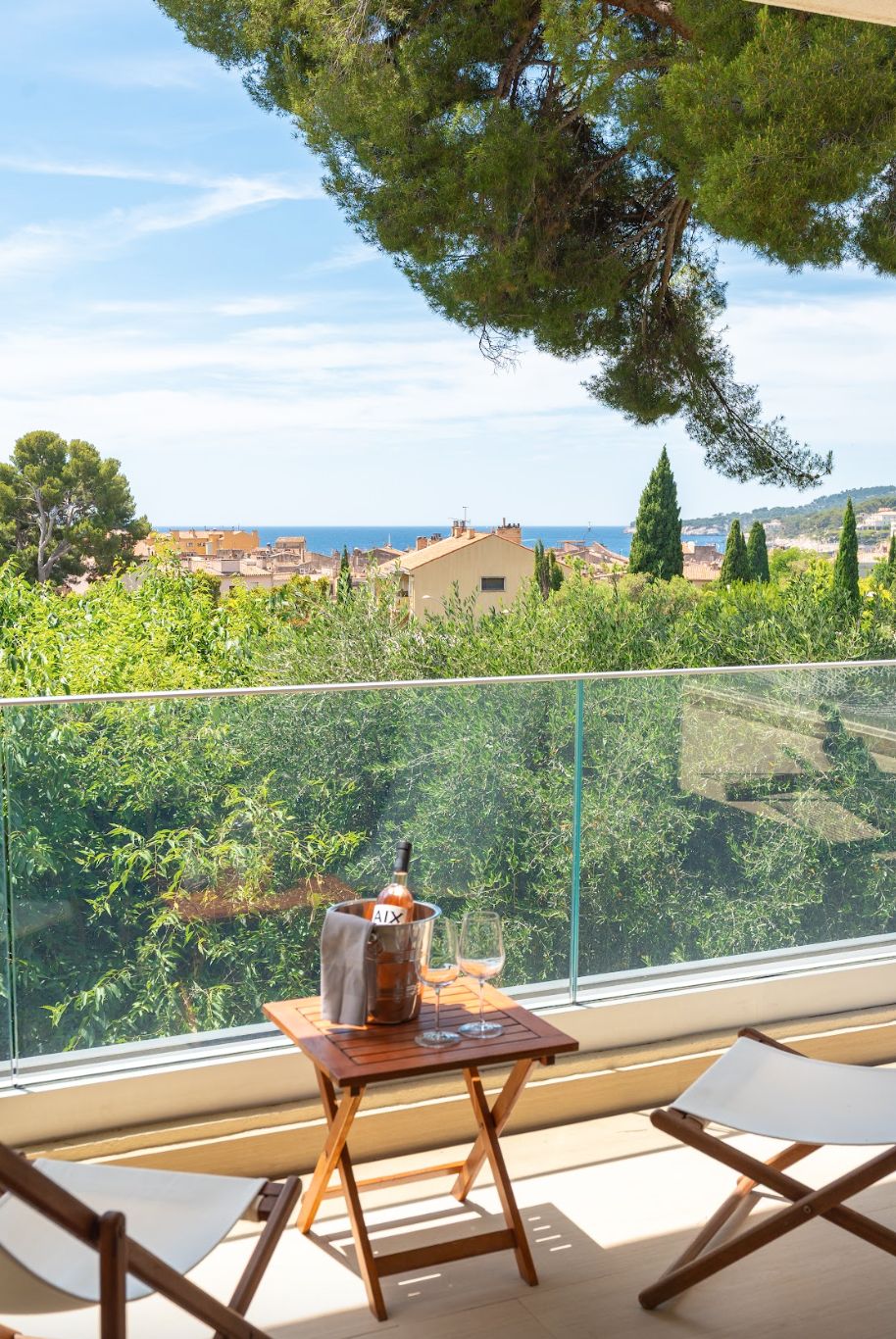 A balcony with a table, a bottle, and glasses, overlooking a coastal town.