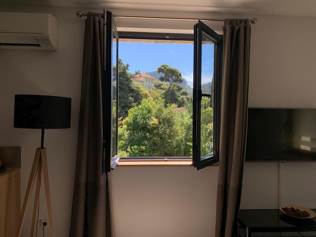 A room with an open window, a tripod lamp, and a flat-screen TV.