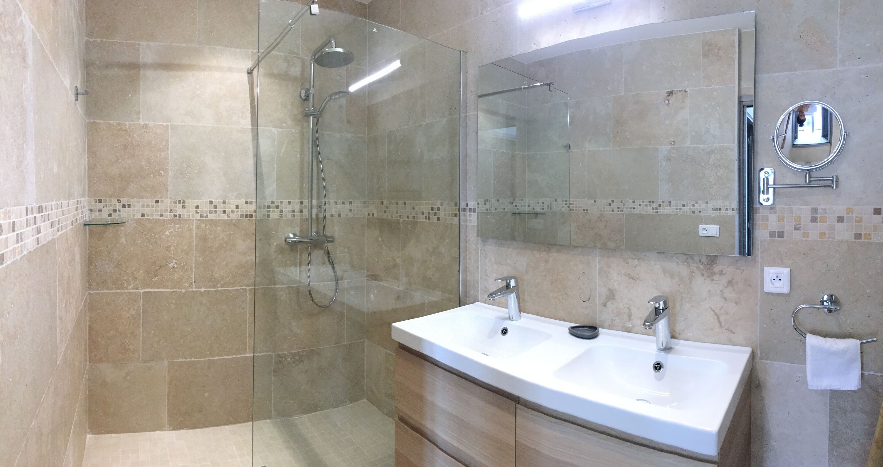 Een moderne badkamer met een douchecabine, een grote spiegel en een dubbele wastafel met een handdoekhouder.