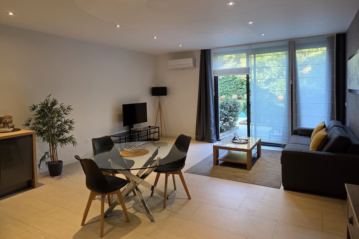 A modern living room with a glass dining table, black chairs, a sofa, and a TV.