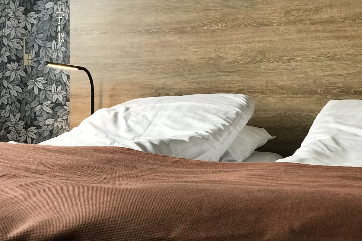 A bed with white pillows and a brown blanket, a wooden headboard, and a floral-patterned curtain.