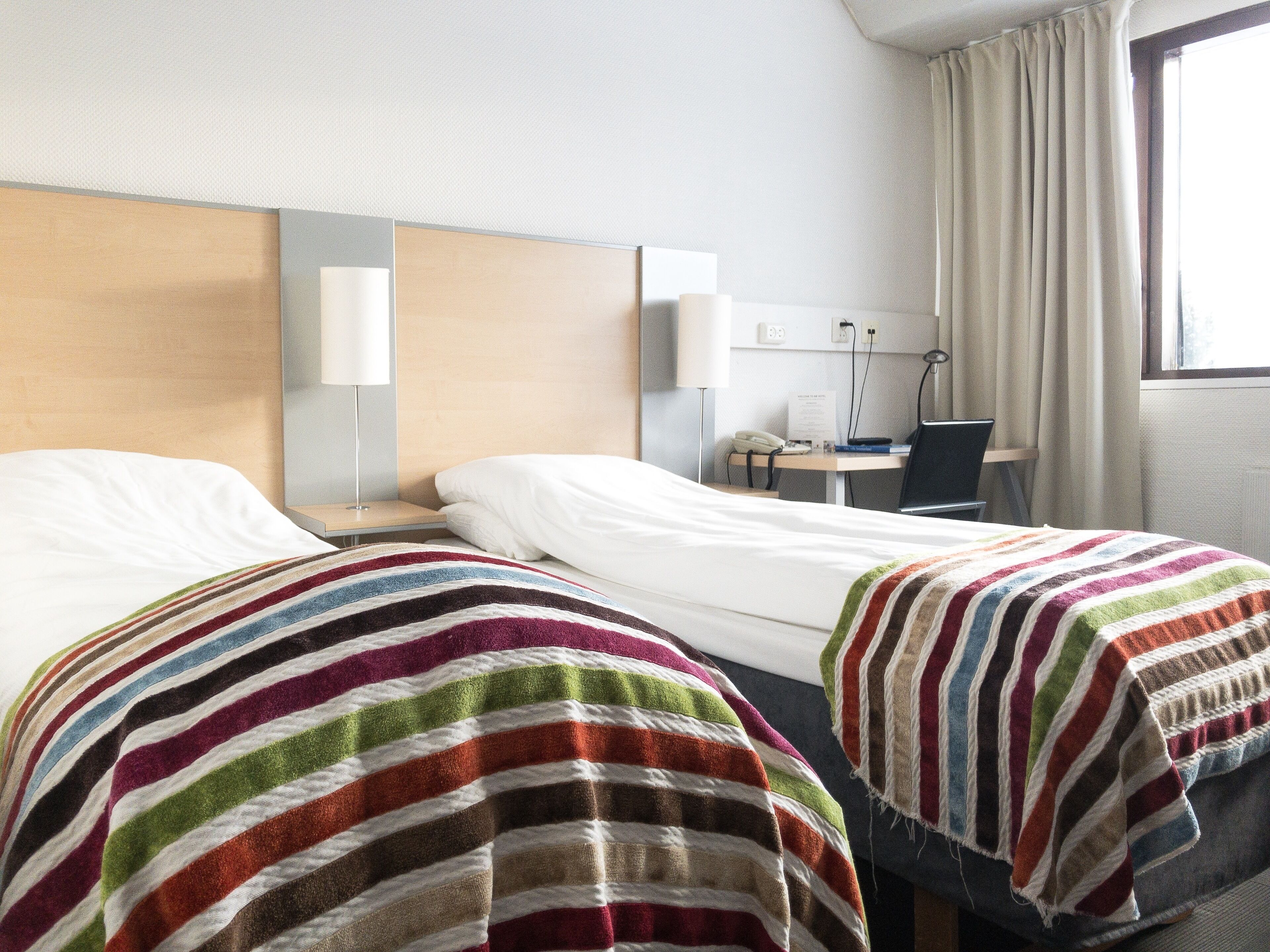 Une chambre d’hôtel avec deux lits, un bureau, une chaise et une fenêtre avec des rideaux.