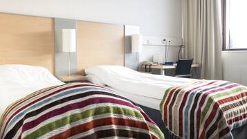 Une chambre d’hôtel avec deux lits, un bureau, une chaise et une fenêtre avec des rideaux.