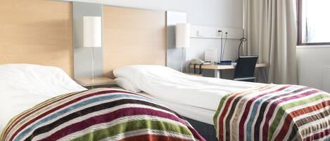 Una habitación de hotel con dos camas, un escritorio, una silla y un ventanal con cortinas.