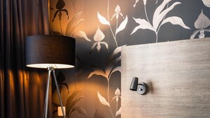 A hotel room with a bed, a floor lamp, a wooden headboard, and a floral wallpaper design.