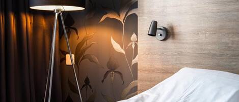 A hotel room with a bed, a floor lamp, a wooden headboard, and a floral wallpaper design.