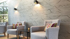 Un interior moderno con sillones tapizados en gris, una pequeña mesa redonda y una pared con diseño de montaña.