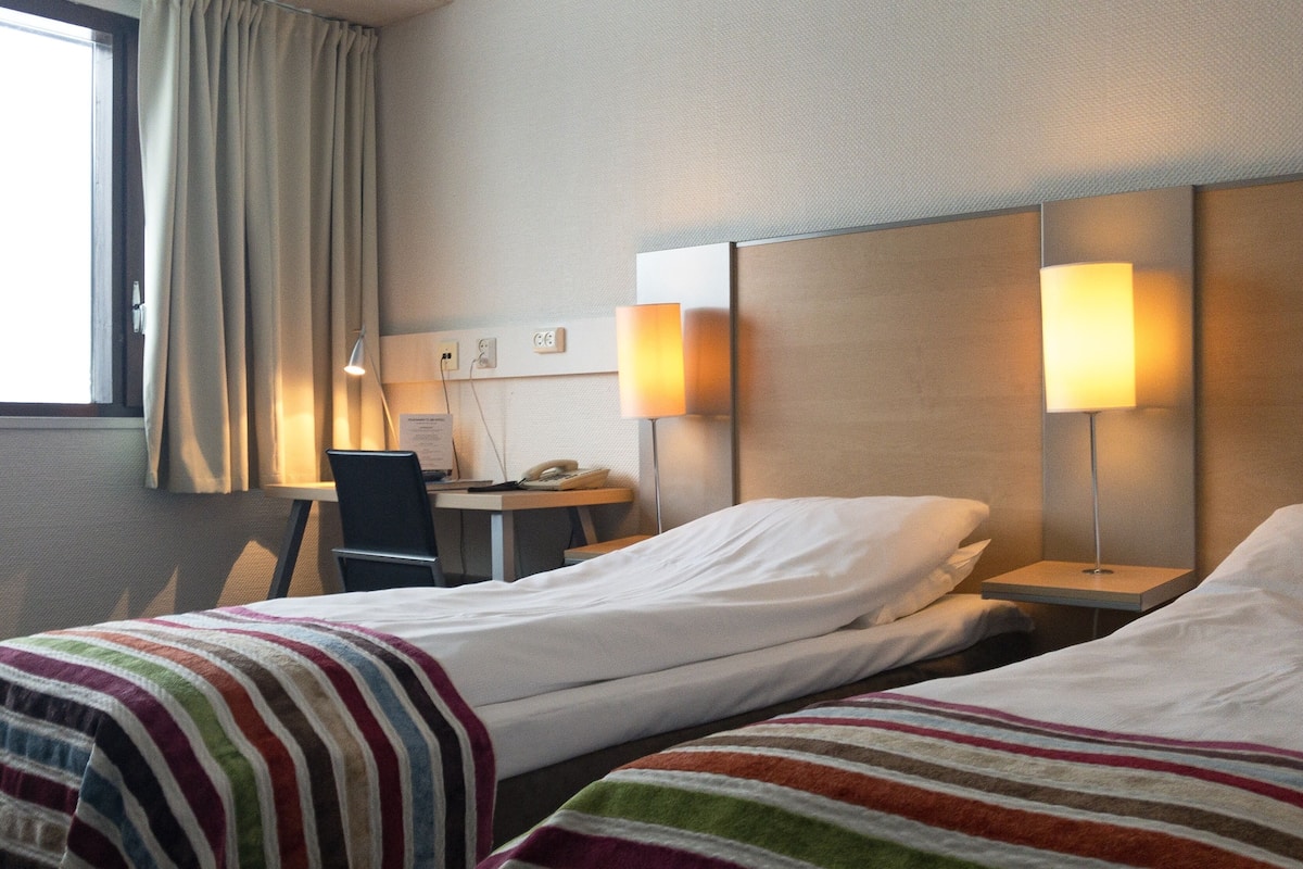 A hotel room with two beds, a desk, a chair, and two bedside lamps.