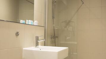 A bathroom with a glass shower enclosure, a white sink, and a mirror above the sink.
