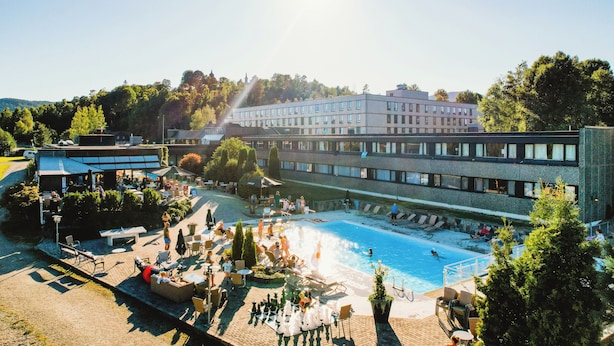 A hotel with a swimming pool, outdoor seating, and a large building in the background.