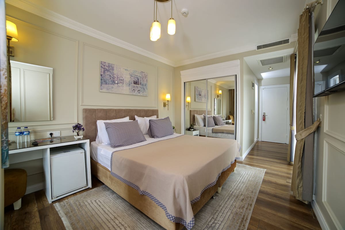 A hotel room with a bed, bedside table, lamp, and a small refrigerator.
