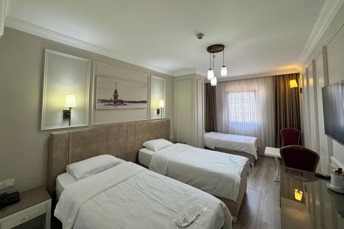A hotel room with two beds, a desk, a chair, a TV, and a painting on the wall.