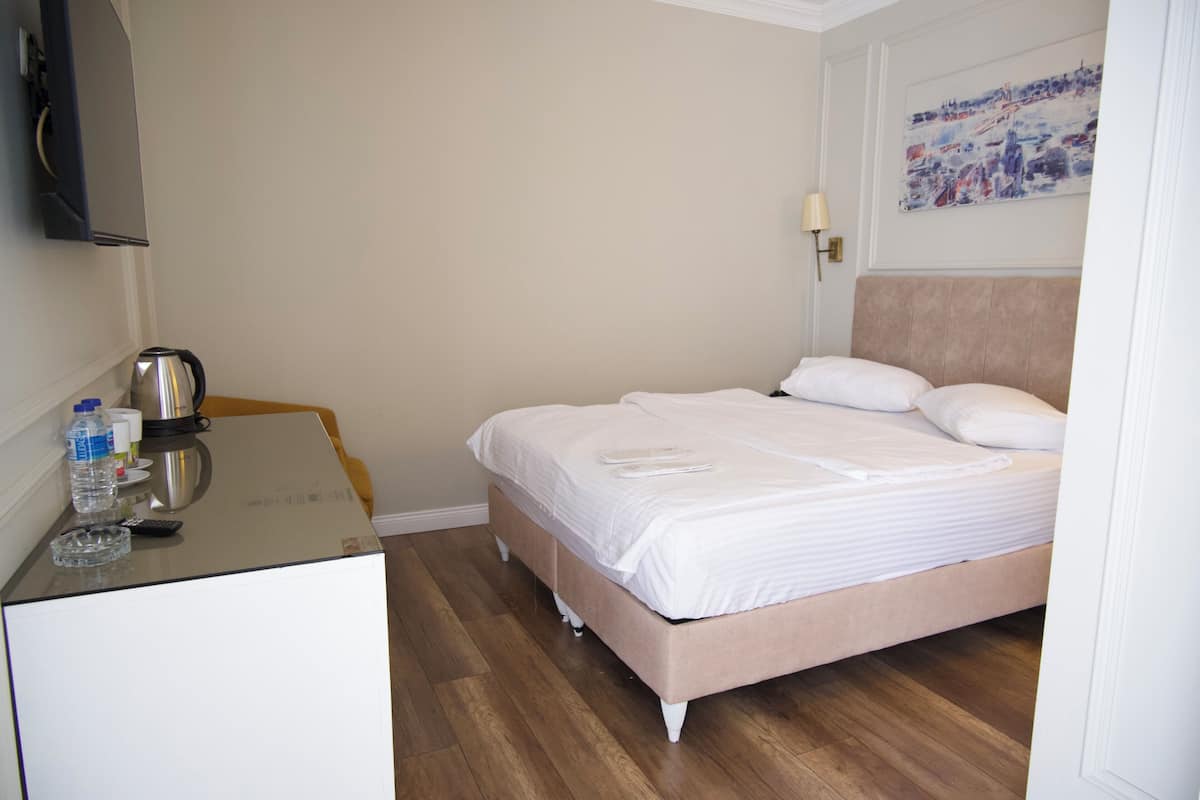 A hotel room with a bed, a desk with a kettle, a bottle of water, and a remote control.