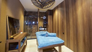A spa room with a wooden bench, a massage table with towels, a large mirror, and a shower area. - Villa Vanilla Hotel  (Istanbul)