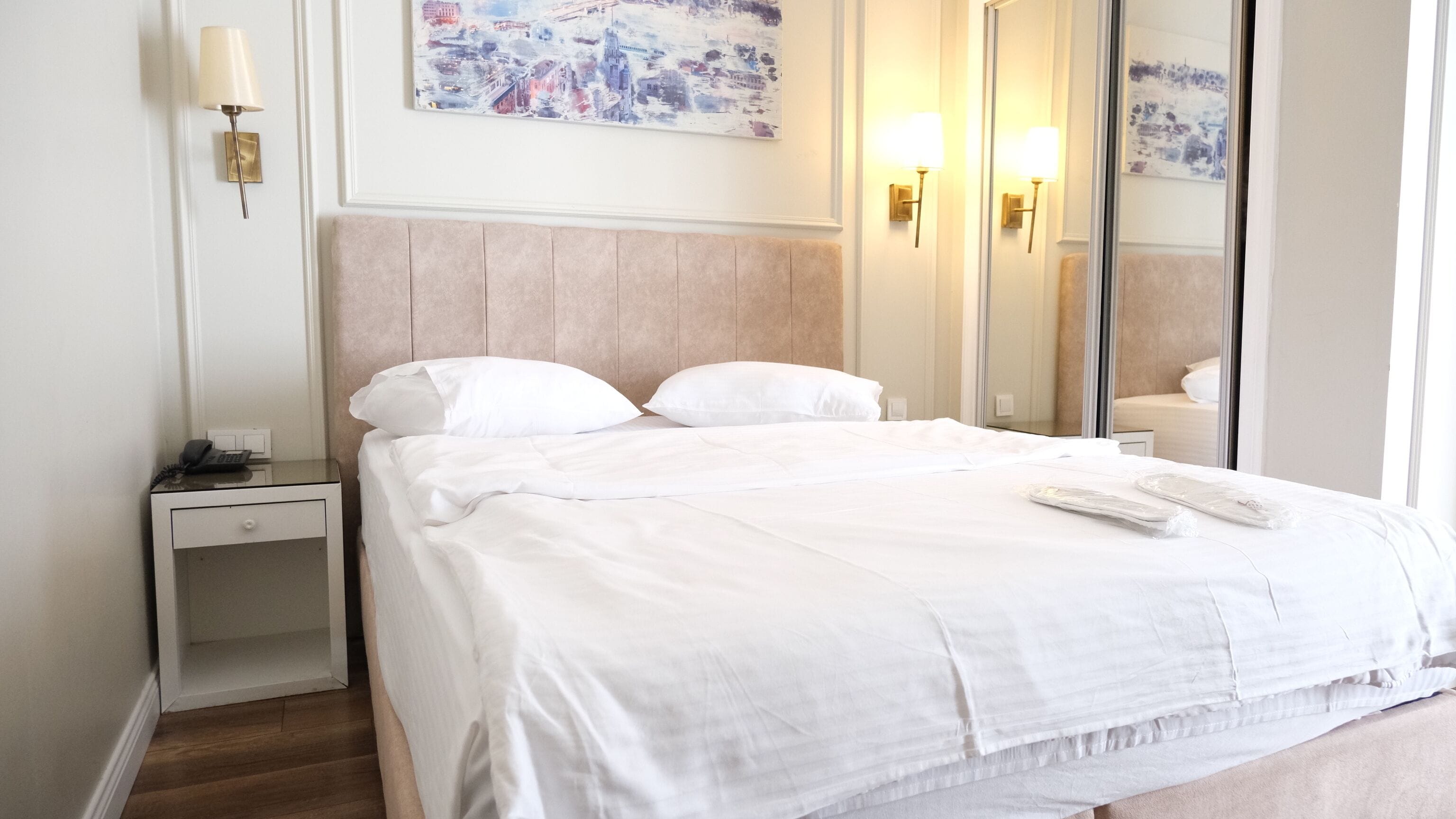 Una habitación de hotel con cama, mesita de noche, lámpara y un cuadro en la pared.