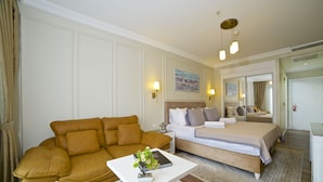 A hotel room with a brown sofa, a white coffee table with a plant, a bed with a white and blue checkered bedspread, and a large mirror above the bed. - Villa Vanilla Hotel  (Istanbul)
