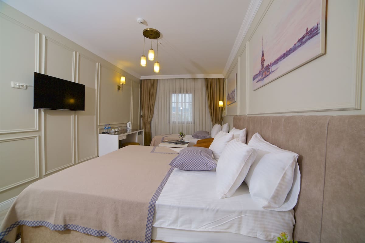 A hotel room with a large bed, a television, a desk with a chair, and a window with curtains.