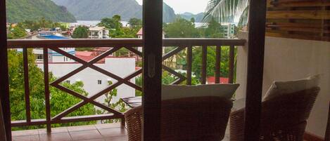A balcony with wicker furniture, a view of a mountainous landscape, and a body of water.