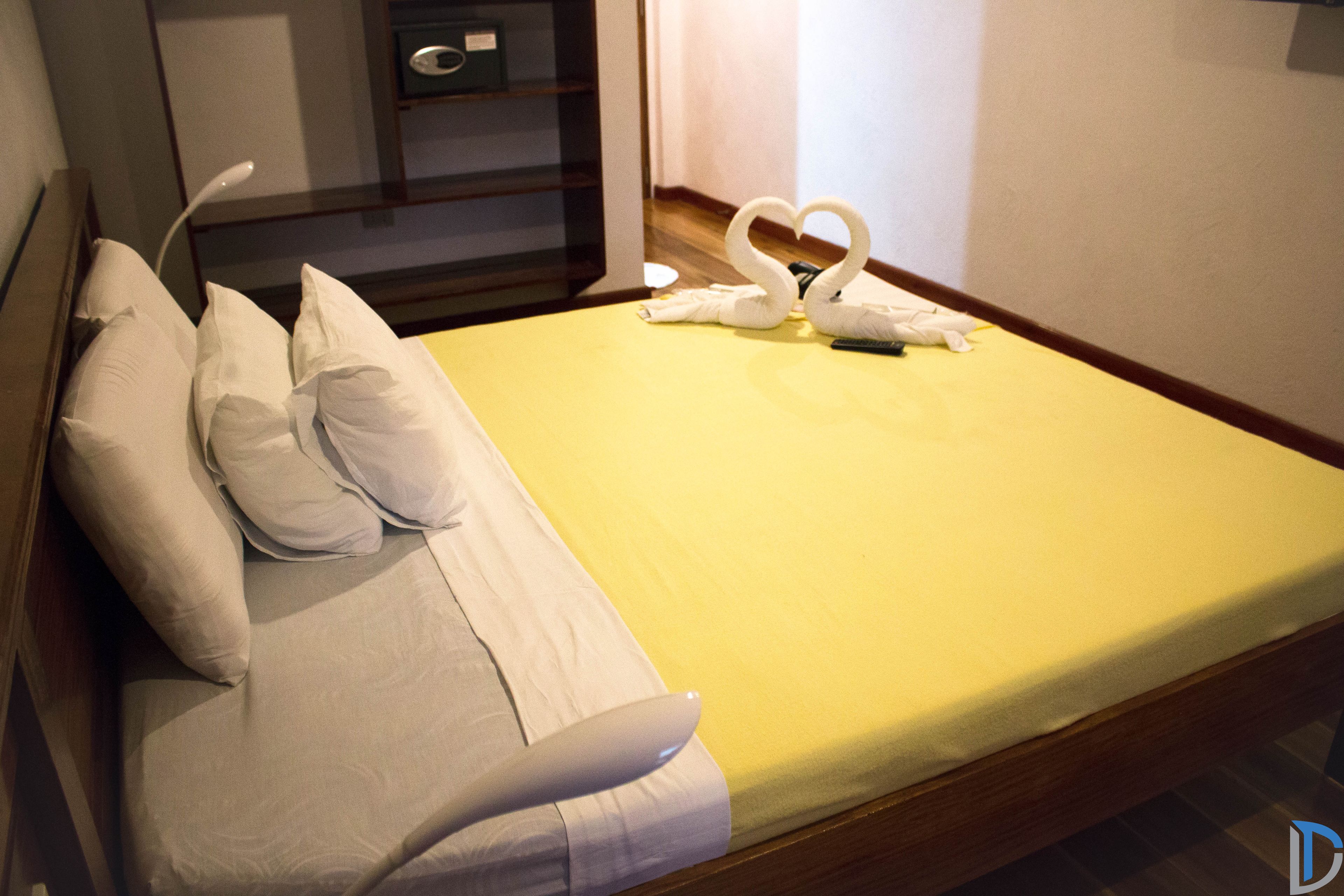 A hotel room with a bed, pillows, a yellow bedspread, and a swan-shaped towel arrangement.