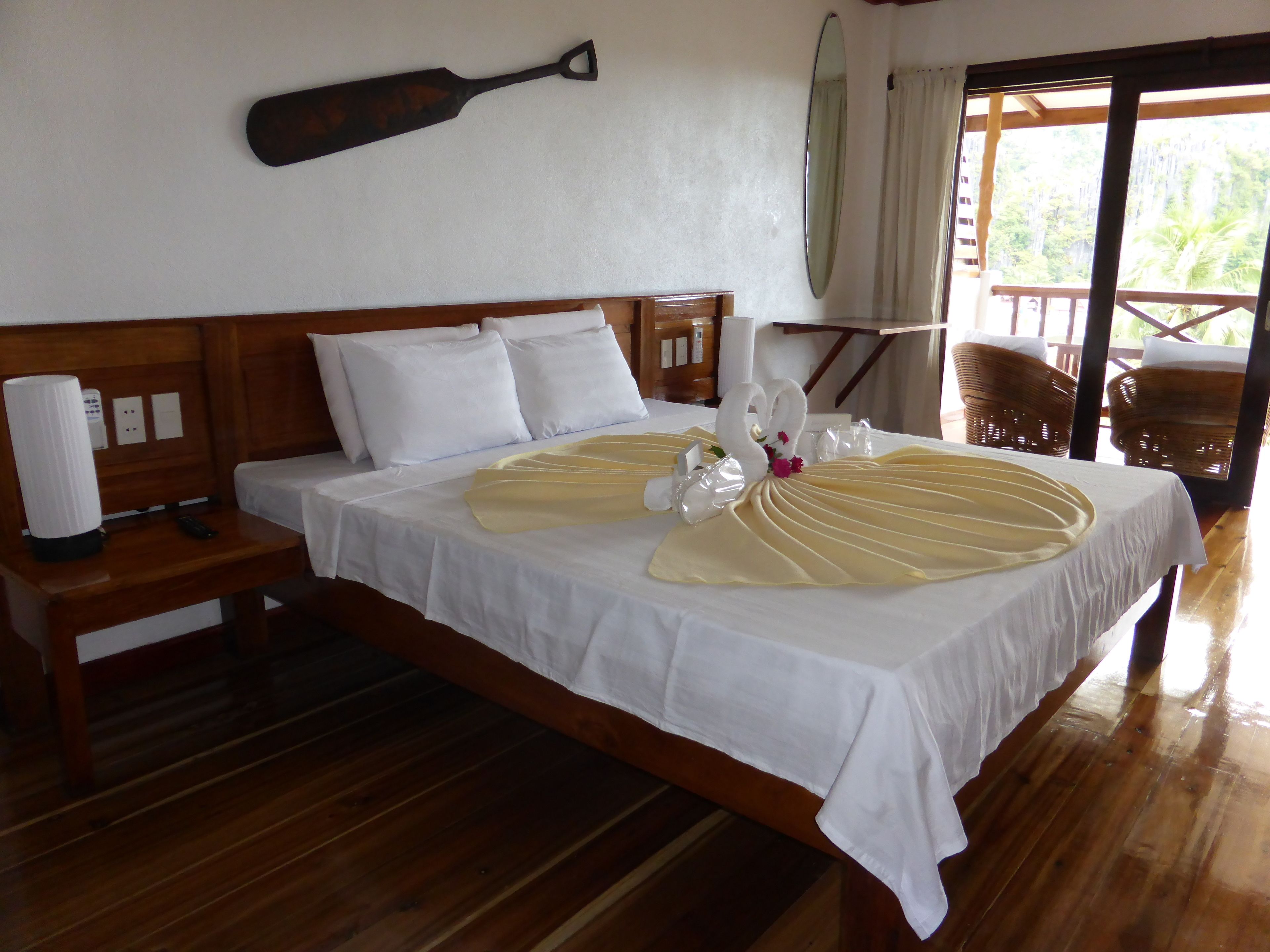 Habitació d'hotel amb llit de fusta, roba de llit blanca, un centre de taula decoratiu amb un cigne i una paleta de fusta a la paret.
