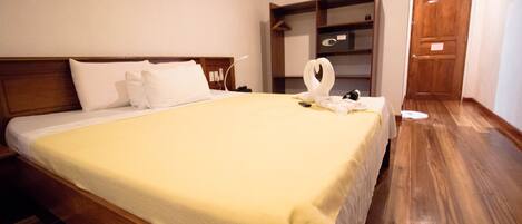 A neatly made bed with a yellow bedspread, a wooden headboard, and a white pillow. There is a wooden shelf unit with a towel and a white swan-shaped towel holder on the bed.