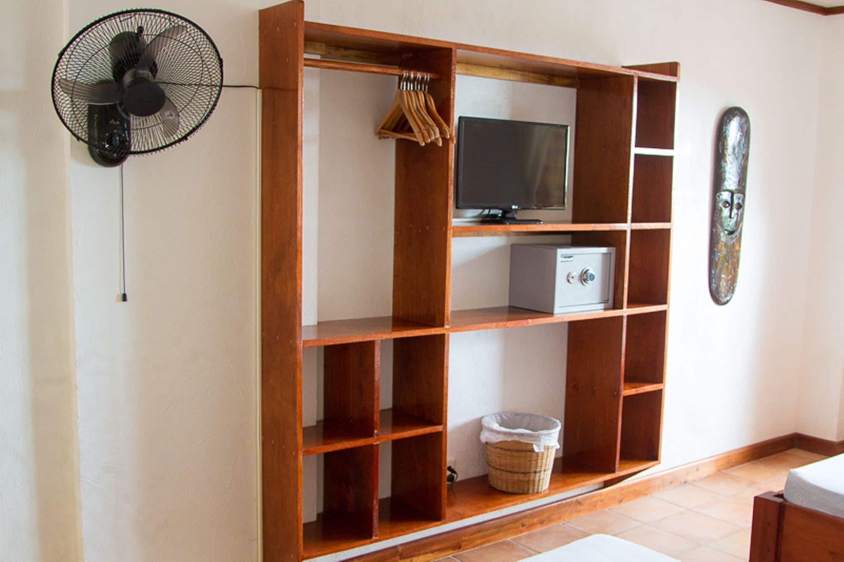 Une pièce avec une étagère en bois, un téléviseur, un ventilateur et un objet décoratif accroché au mur.