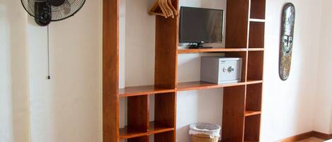 Una habitación con una estantería de madera, un televisor, un ventilador y un objeto decorativo en la pared.