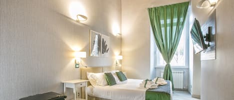 Quarto com cama, mesas de cabeceira, uma mala e janela com cortinas verdes.