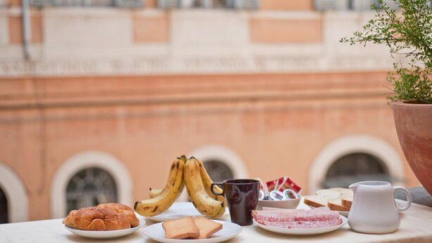 A breakfast table with croissants, bananas, toast, a mug, and a pitcher on a tablecloth. - History Suite (Rome)