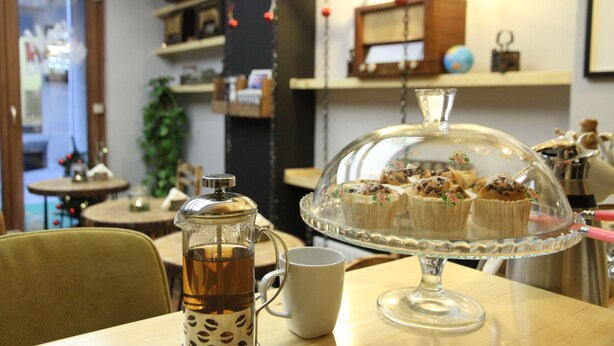 A table with a coffee pot, a mug, and a glass cake stand with cupcakes. - Stay Inn Taksim Hostel (Istanbul)