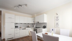 A modern kitchen with white cabinets, a microwave, stove, and a dining area with a white table and chairs. - Heart of Vienna Residence (Vienna)